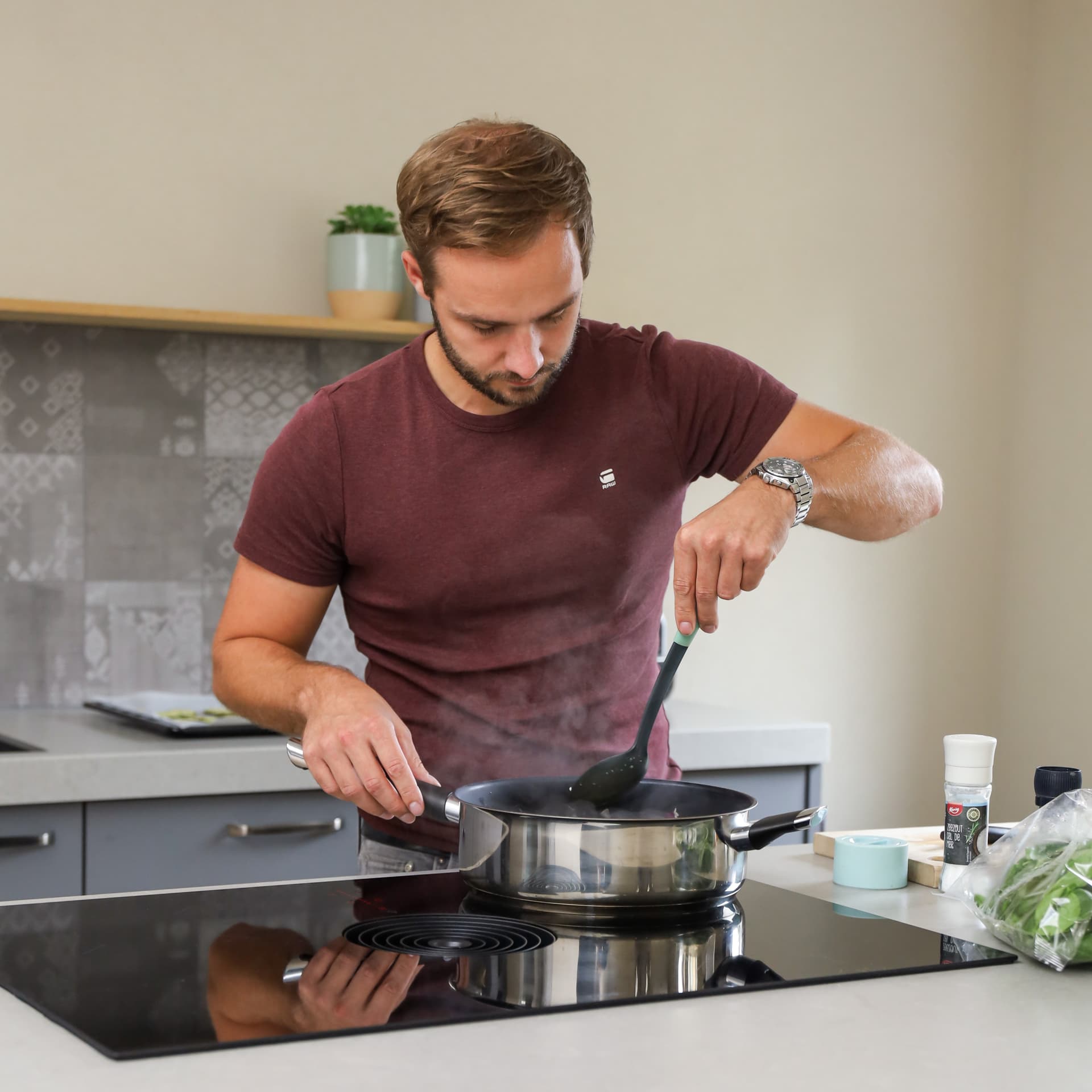 De keuken van rick en minouk_00022.jpg Jonge man aan het koken op kookeiland in grijze keuken