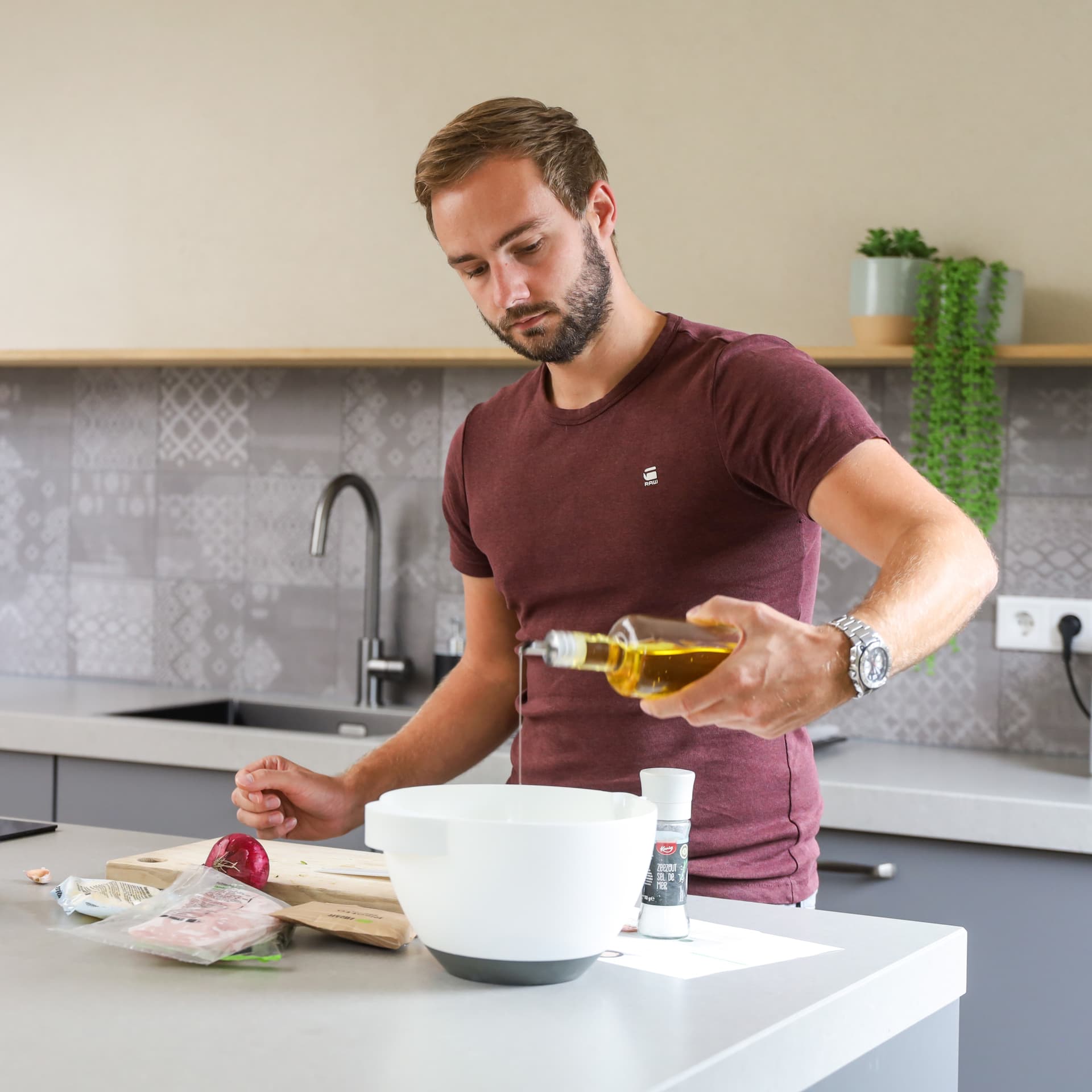 De keuken van rick en minouk_00019.jpg Jonge man die olijfolie over salade giet in een grijze keuken