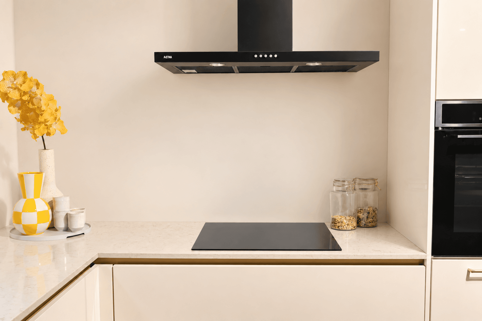 eilandkeuken-paton-magnolia-afzuiger.png Zwarte afzuiger en kookplaat in magnolia kleurige keuken