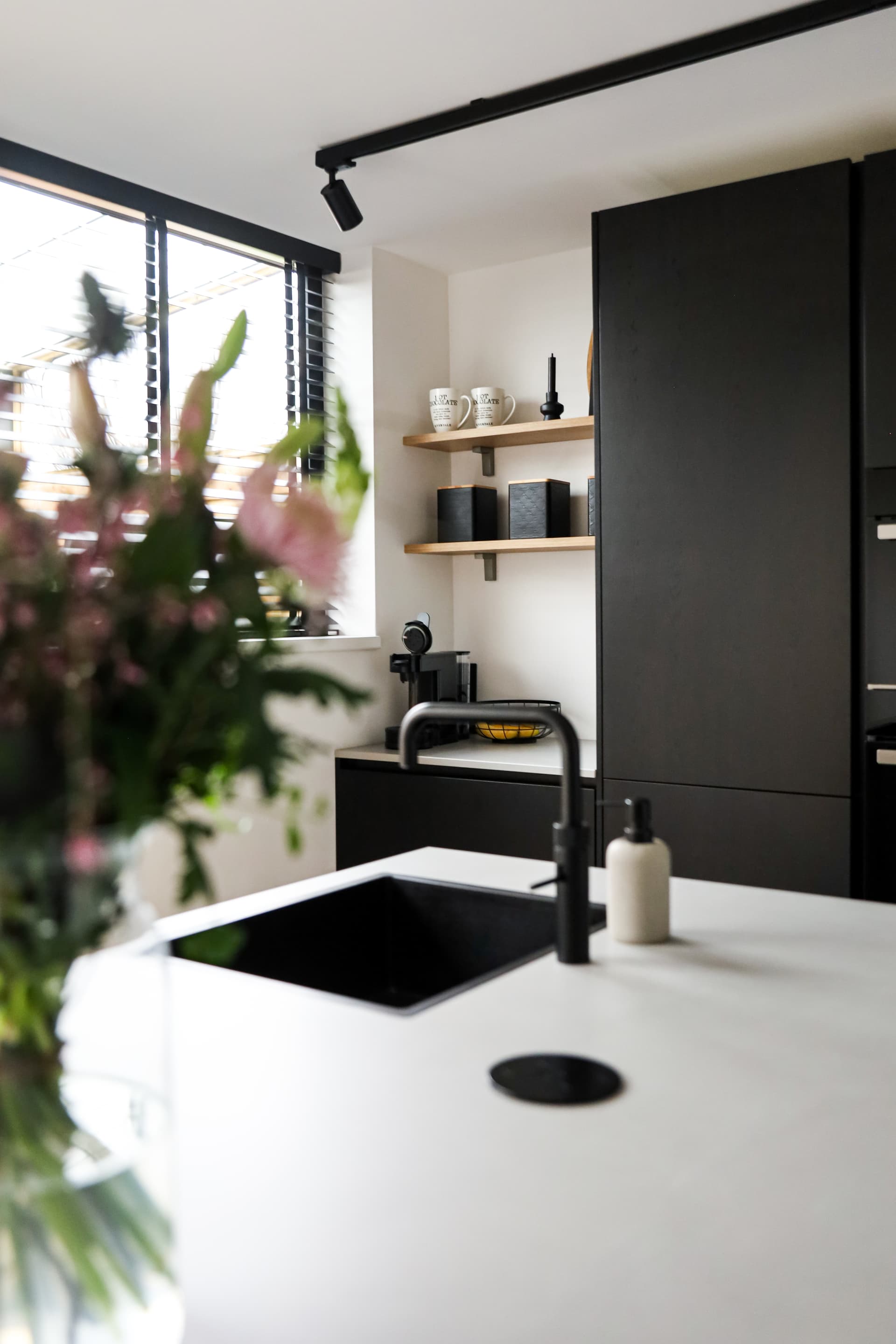 De keuken van Familie van Hooft_00024.jpg Zwarte keuken met kookeiland en een betonlook werkblad waarop een bos bloemen staat